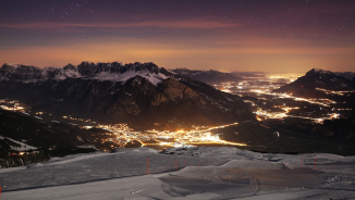View of wintry Sarganserland at night. A ski slope can be seen in the foreground. In the valley you can see the colorful lights.