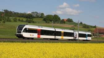 Train with 3 carriages travels through a spring landscape in Switzerland