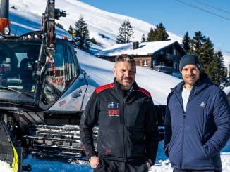 Pistenbully driver Peter Thut stands with presenter Manuel Rothmund in front of Pistenbully in the snow