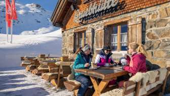 Three friends enjoy coffee on the sun terrace of the Gruebhütte